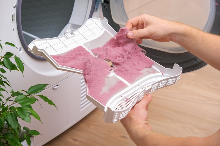 A person removes lint from a lint trap on a dryer